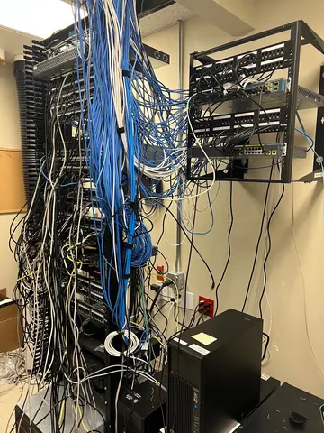 Before: network closet with patch cables hanging loose across the floor rack and wall-mounted rack