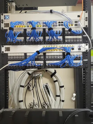 Small open-frame network rack with patch panels, switches and neatly bundled blue cabling